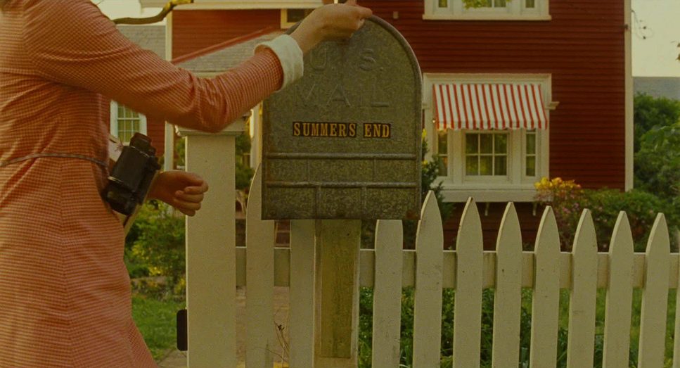Fotograma de Moonrise Kingdom en el que aparece un buzon de correo y una chuca con unos prismáticos abriéndolo.