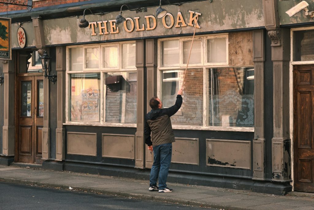 Fotograma de The old oak, donde un hombre arregla el letrero de un bar, al que se le ha caído una letra.