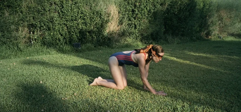 Una chica en bañador gatea por un jardín con los ojos tapados. Fotograma de la película Canino.